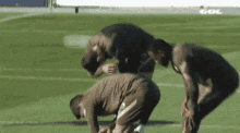 a group of men are squatting down on a soccer field with gol written on the fence in the background