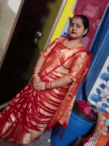 a woman in a red and gold striped saree stands next to a blue barrel