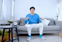 a man in a blue sweater sits on a couch next to a table with a glowienka book on it