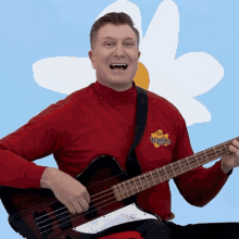 a man wearing a red shirt that says wiggles on it is playing a guitar