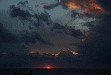 a sunset over the ocean with a dark cloudy sky