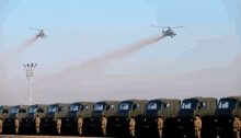 a row of military vehicles are parked in front of a helicopter