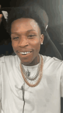 a young man wearing a white shirt and gold chains is smiling