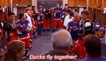 a group of hockey players are standing in a locker room and a man is sitting in front of them .