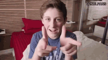 a young boy is making a gun sign with his hands while sitting on a bed in a bedroom .