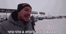 a man wearing a beanie that says ' steel ' on it smiles in front of a snowy parking lot