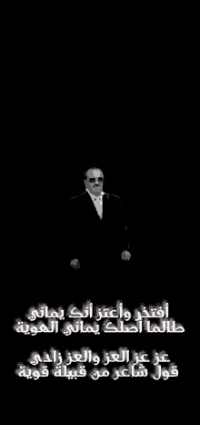 a man in a suit and tie stands in front of a black background with arabic writing