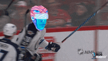 a hockey player is wearing a mask and holding a stick with the nhl logo behind him