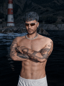 a shirtless man with a snake tattoo on his arm stands in front of a lighthouse