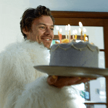 a man in a white fur coat is holding a cake with candles