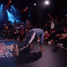 a man in a blue shirt is doing a trick on a stage with a crowd watching and a sign that says b-boy