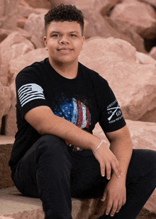 a young man in a black shirt is sitting on a rock .