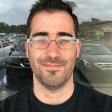 a man with glasses and a beard smiles in front of a parking lot