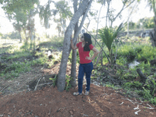 a woman in a red shirt leans against a tree in the woods