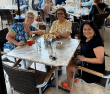 two women are sitting at a table with a drink in their hand