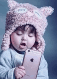 a baby wearing a pink owl hat is holding an apple iphone .