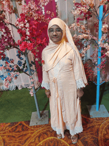 a woman wearing a hijab and glasses stands in front of a tree with pink flowers