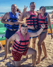 a group of people wearing life jackets pose for a photo on the beach