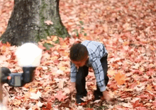 a young boy is playing in a pile of leaves while a camera is taking a picture of him .