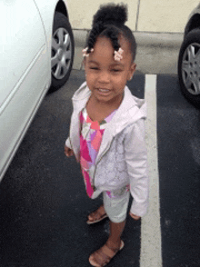 a little girl is standing in a parking lot next to a car