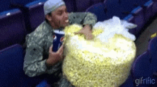 a man in a military uniform is eating a large bag of popcorn while holding a cup of pepsi .