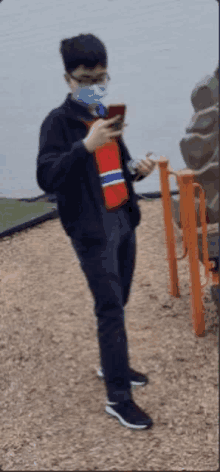 a young man wearing a mask and glasses is standing in a playground .