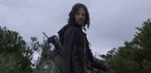 a man with long hair is holding a bow and arrow in a forest