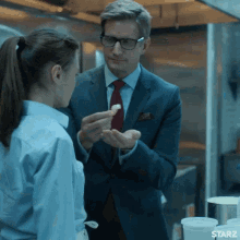 a man in a suit and tie is giving a piece of food to a woman in a kitchen with starz written on the bottom