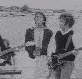 a black and white photo of a group of men playing guitars in front of a body of water .