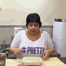 a woman wearing a white shirt with the word pretty on it is sitting at a table with a container of food .