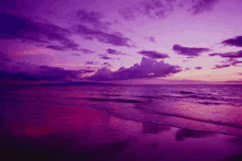 a purple sunset over a beach with waves crashing against the shore .