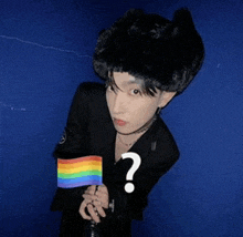 a person holding a small rainbow flag with a question mark on their chest