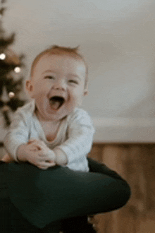 a baby is sitting on a person 's lap and laughing with his mouth open .