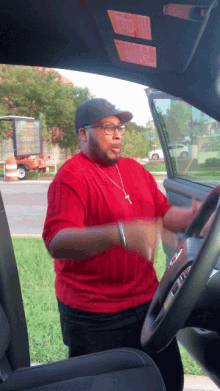 a man in a red shirt is dancing in a car with a sticker on the windshield that says airbag