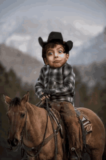 a young boy wearing a cowboy hat is riding a brown horse