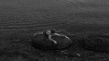 a man is laying on a rock in the water .