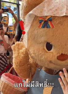 a teddy bear with a rainbow bow on its head is standing in front of a crowd