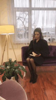 a woman in a black dress sits on a purple couch holding a book