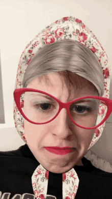 a woman wearing glasses and a floral head scarf makes a face