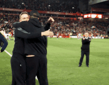 two men hugging on a soccer field with a crowd in the background and a sign that says ' champions '