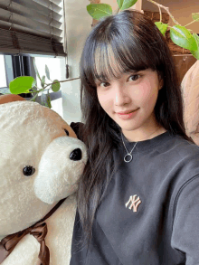 a girl wearing a black ny sweatshirt holds a teddy bear