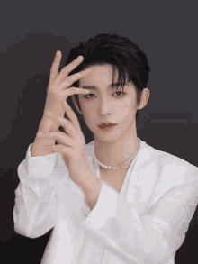 a young man wearing a white shirt and a pearl necklace is making a gesture with his hands