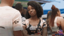 a woman in a floral top stands with her arms crossed in front of a man in a white shirt with the word chi on it