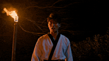 a man in a white karate uniform holds a torch in his hand