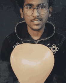 a man wearing glasses holds a heart shaped balloon