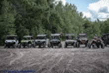 a group of atvs are parked in a row on a dirt road in the woods .