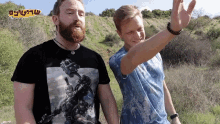 two men are standing in a field and one has a t-shirt with a picture of a soldier on it