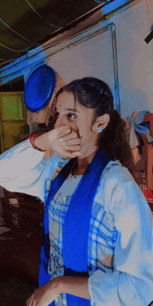 a woman covering her mouth with her hand while wearing a blue and white dress