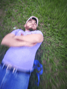 a man in a purple shirt is laying in the grass with his arms crossed