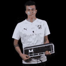 a man wearing a white shirt that says alienware is holding a keyboard